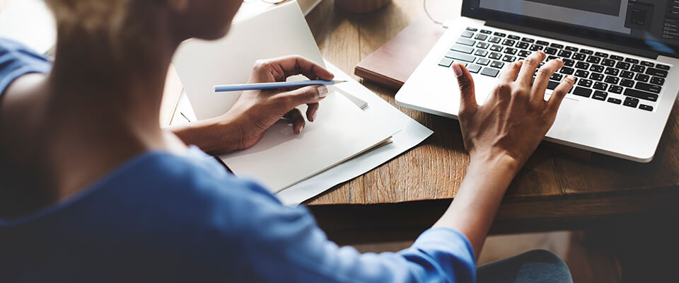 Woman taking notes and working on laptop